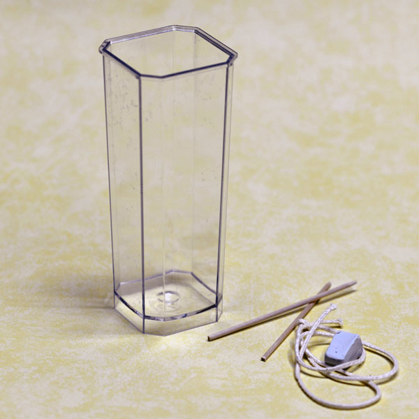 Transparente eckige Kerzen-Gießform quadratisch 48x48x140mm mit beiliegendem Docht und Knetmasse auf weißem Hintergrund.
